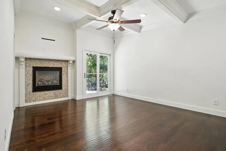 Unfurnished living room with coffered ceiling, a fireplace, beam ceiling, dark wood finished floors, and crown molding