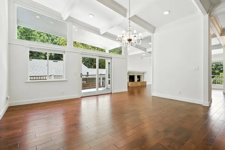 Unfurnished living room with beamed ceiling, coffered ceiling, a fireplace with raised hearth, dark wood-style floors, and a chandelier