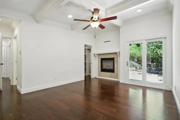 Unfurnished living room featuring coffered ceiling, beamed ceiling, a glass covered fireplace, dark wood-style floors, and a ceiling fan