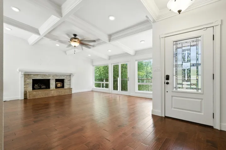 Unfurnished living room featuring coffered ceiling, beamed ceiling, dark wood-style floors, ornamental molding, and a fireplace with raised hearth
