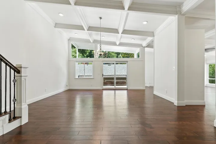 Unfurnished living room featuring dark wood-style floors, beamed ceiling, stairs, ornamental molding, and coffered ceiling