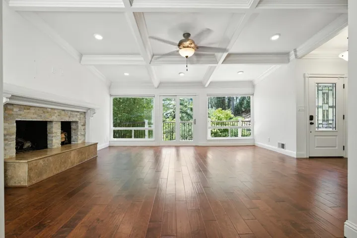 Unfurnished living room featuring a fireplace, dark wood-type flooring, coffered ceiling, beamed ceiling, and ceiling fan