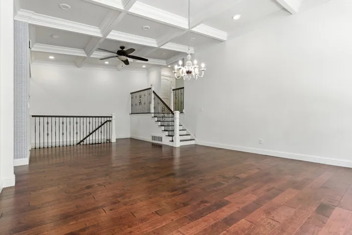 Unfurnished living room featuring coffered ceiling, beam ceiling, dark wood-style flooring, a chandelier, and stairway