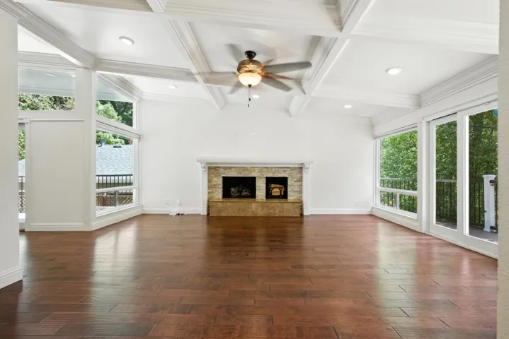 Unfurnished living room with a fireplace with raised hearth, crown molding, dark wood finished floors, coffered ceiling, and beam ceiling