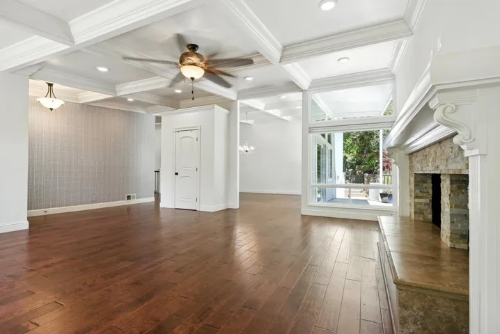 Unfurnished living room featuring coffered ceiling, beamed ceiling, dark wood-type flooring, a chandelier, and a stone fireplace