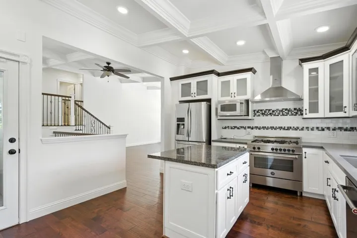 Kitchen with coffered ceiling, beam ceiling, stainless steel appliances, wall chimney range hood, and glass insert cabinets
