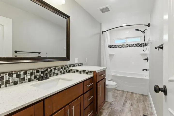 Bathroom featuring shower / bathtub combination with curtain, light wood finished floors, vanity, and backsplash