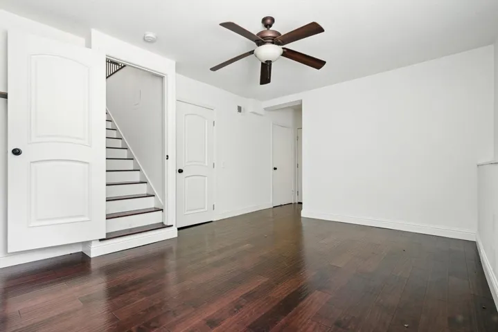 Unfurnished living room with ceiling fan, dark wood-style flooring, and stairway