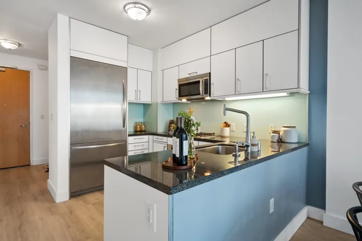 Open-concept kitchen featuring dark stone countertops, re-engineered wood flooring updated in 2024, track lighting, and light wood finishes. Equipped with a stainless steel Bosch dishwasher (2024), Thermador refrigerator, and Miele washer and dryer (2023)