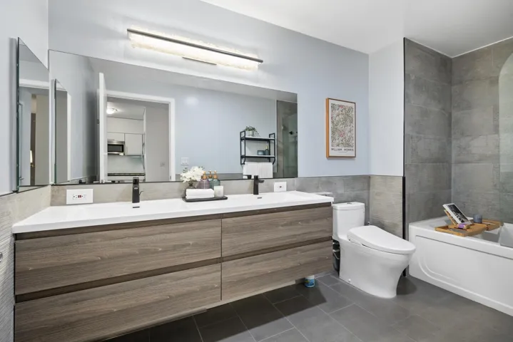 Bathroom updated in 2024 featuring tile walls, slate tile flooring, dual-sink vanity, and shower/bath combination. Dual sinks are a rare upgrade, as most units originally have one sink.