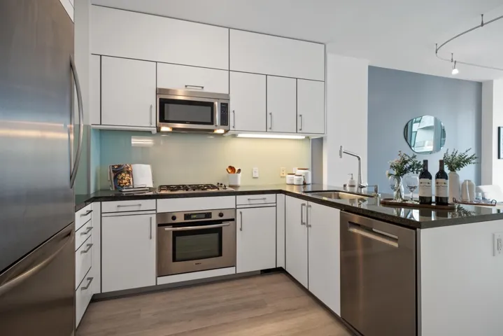 Open-concept kitchen featuring dark stone countertops, re-engineered wood flooring updated in 2024, track lighting, and light wood finishes. Equipped with a stainless steel Bosch dishwasher (2024), Thermador refrigerator, and Miele washer and dryer (2023)