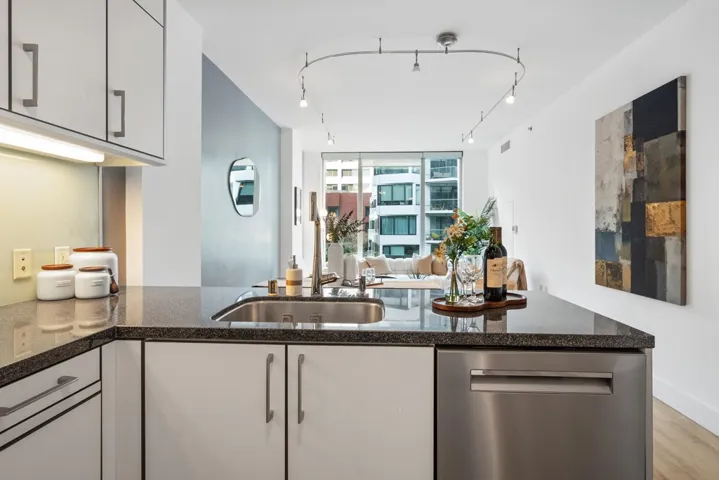 Open-concept kitchen featuring dark stone countertops, re-engineered wood flooring updated in 2024, track lighting, and light wood finishes. Equipped with a stainless steel Bosch dishwasher (2024), Thermador refrigerator, and Miele washer and dryer (2023)