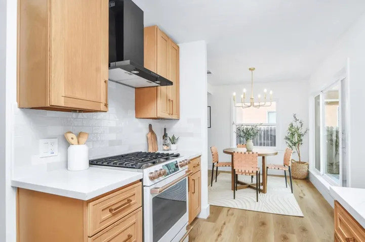 Kitchen with white gas stove, wall chimney exhaust hood, a chandelier, light wood-type flooring, and light brown cabinetry
