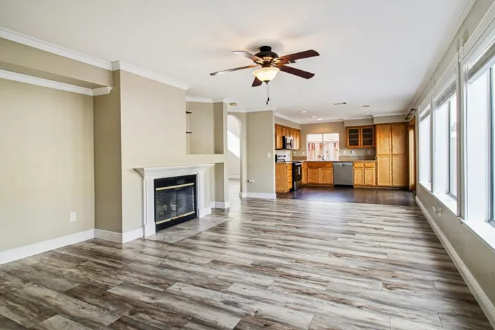 Unfurnished living room featuring a glass covered fireplace, dark wood-style floors, crown molding, and a ceiling fan