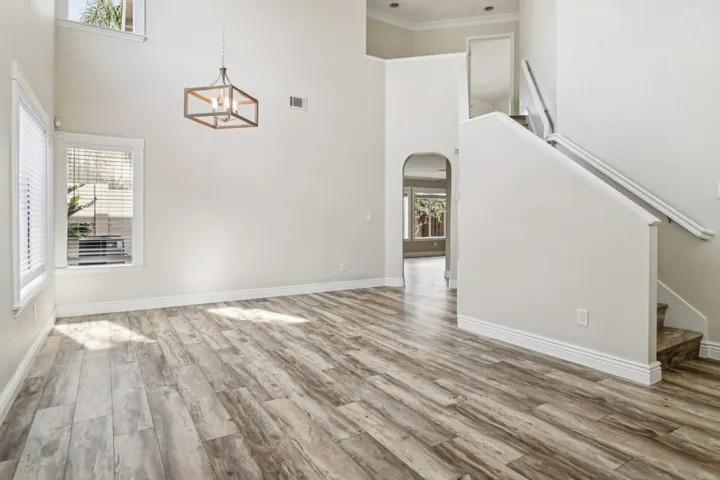Unfurnished living room featuring stairs, a towering ceiling, arched walkways, light wood-style floors, and crown molding