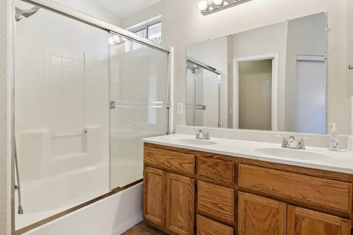 Bathroom featuring double vanity, shower / bath combination with glass door, and a textured wall