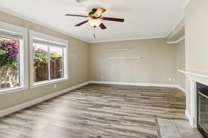 Unfurnished living room with crown molding, a ceiling fan, light wood-type flooring, and a glass covered fireplace