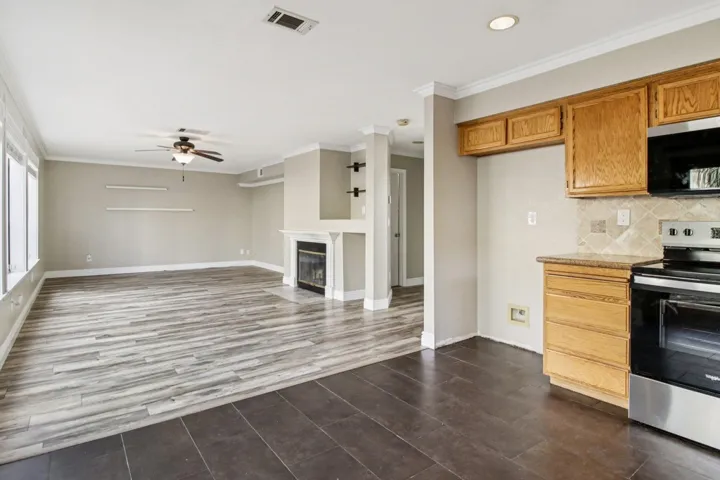 Kitchen with ornamental molding, stainless steel appliances, decorative backsplash, a fireplace with flush hearth, and ceiling fan