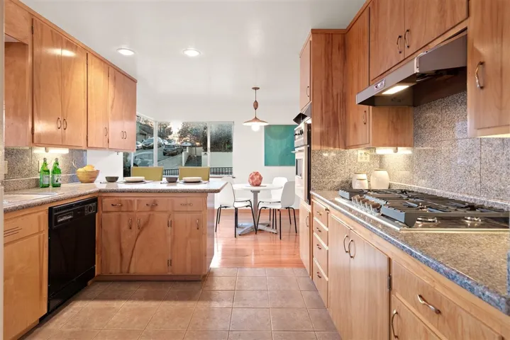 Kitchen with tasteful backsplash, under cabinet range hood, appliances with stainless steel finishes, a peninsula, and pendant lighting
