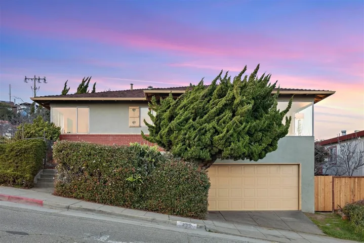 View of property hidden behind natural elements with brick siding, stucco siding, concrete driveway, and an attached garage