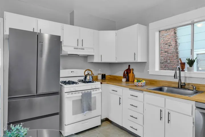 Kitchen with appliances with stainless steel finishes, white cabinets, under cabinet range hood, and light tile patterned floors