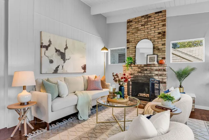 Living room featuring wood finished floors, a brick fireplace, a towering ceiling, and beam ceiling