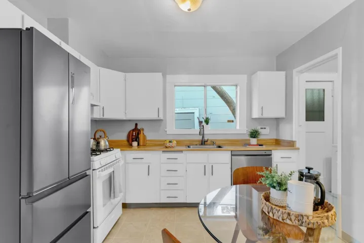 Kitchen with stainless steel appliances, white cabinets, light tile patterned flooring, and butcher block countertops
