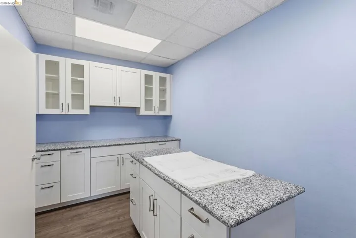 Kitchen with glass insert cabinets, white cabinets, light stone countertops, a drop ceiling, and dark wood finished floors