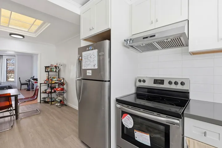 Kitchen with stainless steel appliances, white cabinetry, under cabinet range hood, and crown molding