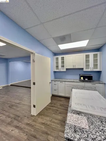 Kitchen with glass insert cabinets, a drop ceiling, white cabinetry, light stone countertops, and dark wood-style floors