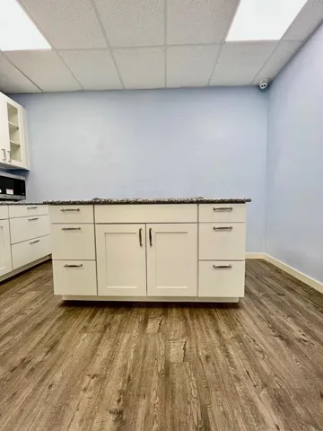 Kitchen with dark wood-style flooring, a drop ceiling, white cabinets, glass insert cabinets, and stainless steel microwave