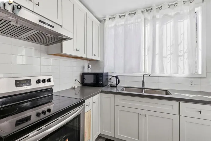 Kitchen with stainless steel electric range, under cabinet range hood, white cabinets, black microwave, and backsplash