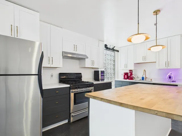 Kitchen featuring white cabinetry, stainless steel appliances, butcher block countertops, decorative light fixtures, and under cabinet range hood