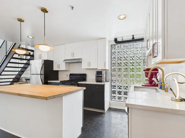 Kitchen featuring white cabinets, finished concrete floors, freestanding refrigerator, black gas range oven, and pendant lighting