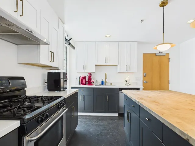 Kitchen with stainless steel appliances, concrete flooring, decorative light fixtures, under cabinet range hood, and white cabinetry