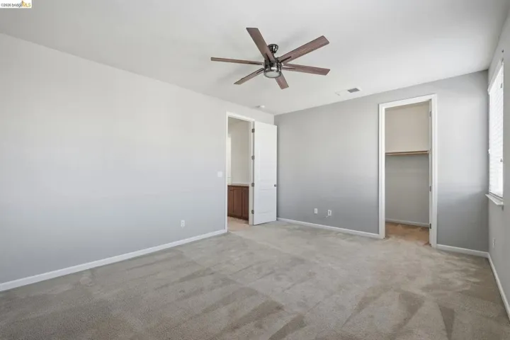 Unfurnished bedroom with a spacious closet, a ceiling fan, and light carpet