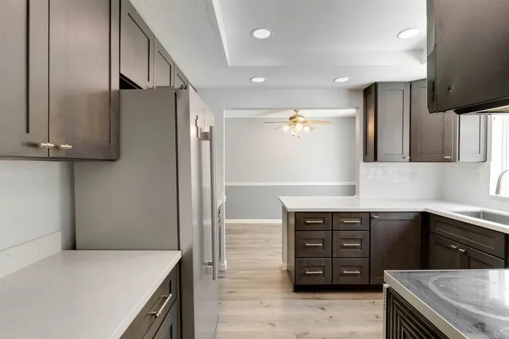 Kitchen with light wood-style floors, freestanding refrigerator, recessed lighting, light stone counters, and tasteful backsplash