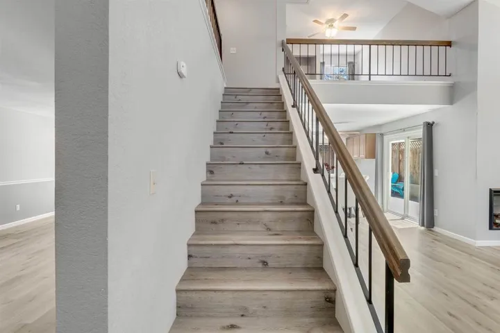 Stairway featuring wood finished floors, a towering ceiling, a textured wall, and a ceiling fan