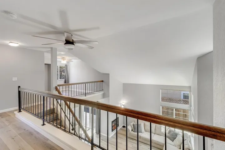 Hallway featuring light wood-style flooring, an upstairs landing, and vaulted ceiling