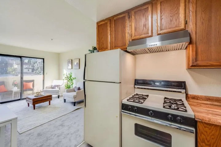 Kitchen featuring white appliances, under cabinet range hood, brown cabinets, and light countertops