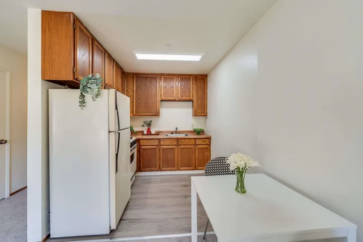 Kitchen with white appliances, brown cabinets, light countertops, and light wood-style flooring