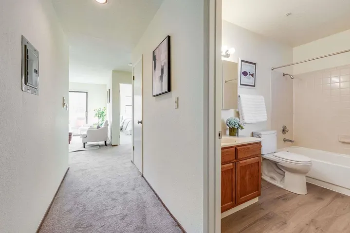 Hall with electric panel, light carpet, light wood finished floors, and a textured wall