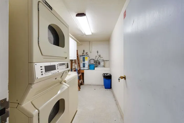 Laundry area with light floors, electric water heater, and estacked washer and dryer