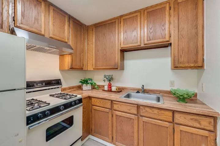 Kitchen with white appliances, under cabinet range hood, light countertops, and brown cabinets