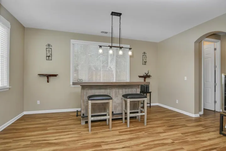 Indoor dry bar featuring arched walkways, light wood-style flooring, pendant lighting, and plenty of natural light