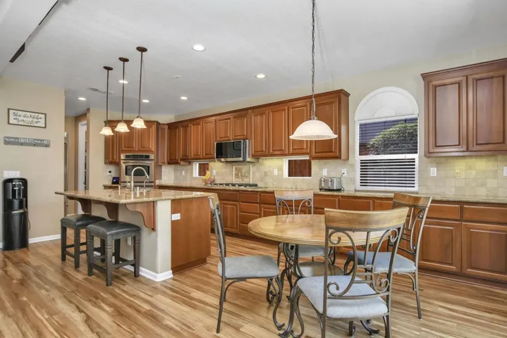 Kitchen featuring a kitchen bar, light stone counters, brown cabinets, a center island with sink, and pendant lighting