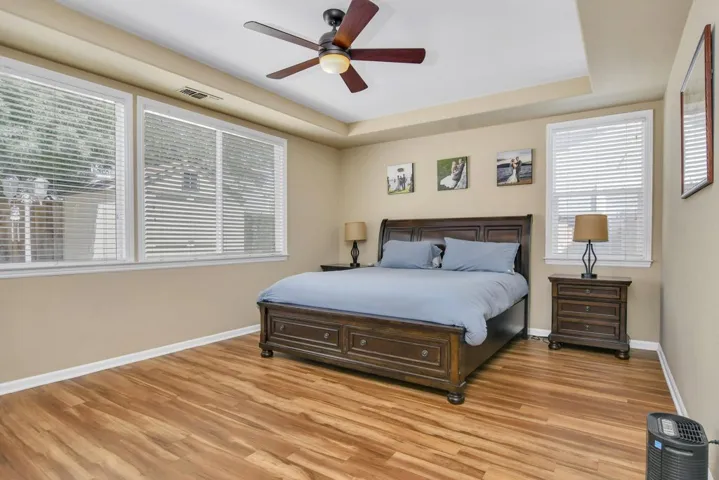 Bedroom with a raised ceiling, a ceiling fan, and light wood-type flooring