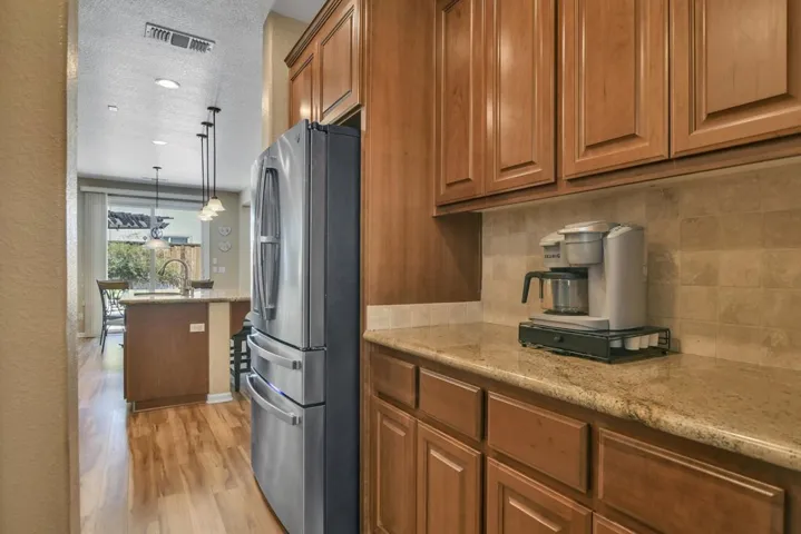 Kitchen with light stone countertops, freestanding refrigerator, brown cabinetry, pendant lighting, and light wood-style flooring