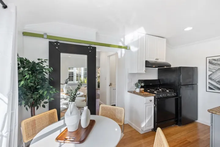 Kitchen with white cabinetry, black appliances, crown molding, under cabinet range hood, and light wood finished floors