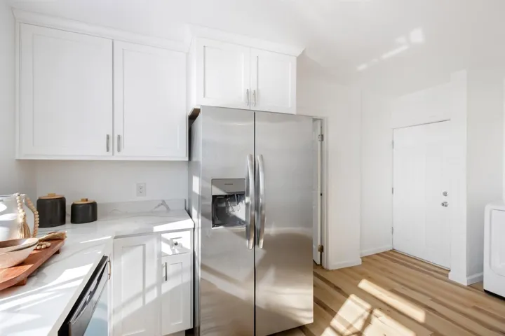 Kitchen featuring appliances with stainless steel finishes, white cabinets, light stone countertops, light wood-style flooring, and washer / dryer